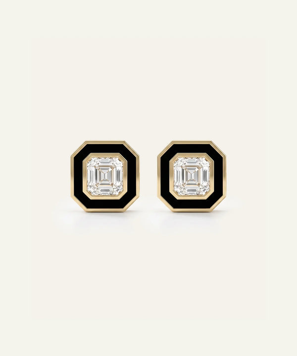 A pair of men's gold-toned stud earrings featuring square Asscher-cut clear central stones framed by black enamel borders, set against a light cream background.