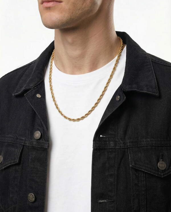 A close-up of a person wearing a gold chain necklace over a white t-shirt and a black denim jacket, against a plain light background.