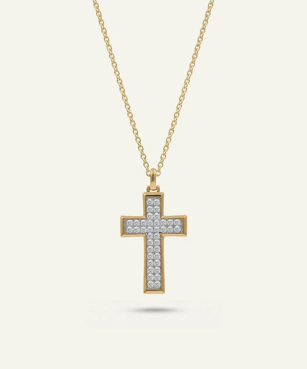 A gold cross pendant necklace adorned with small clear stones, suspended from a delicate gold chain against a light cream background.