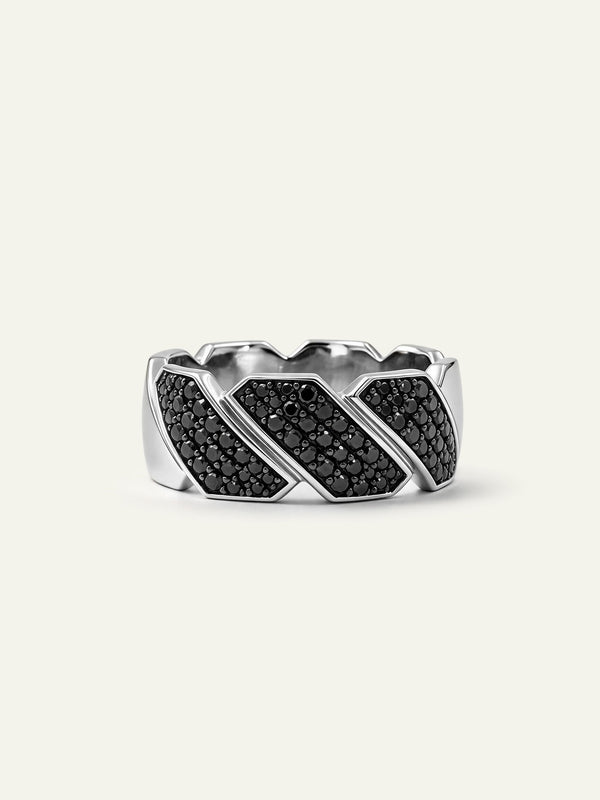 A wide men's silver band ring featuring a geometric, segmented design accented with dark pavé-set black diamonds, displayed on a light cream background.