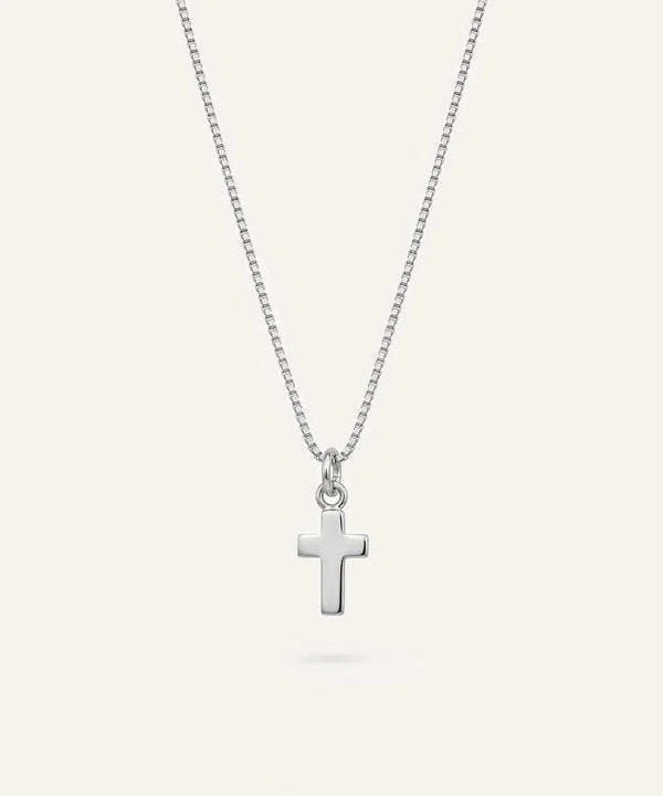 A silver cross pendant necklace on a delicate silver box chain, displayed against a solid off-white background.