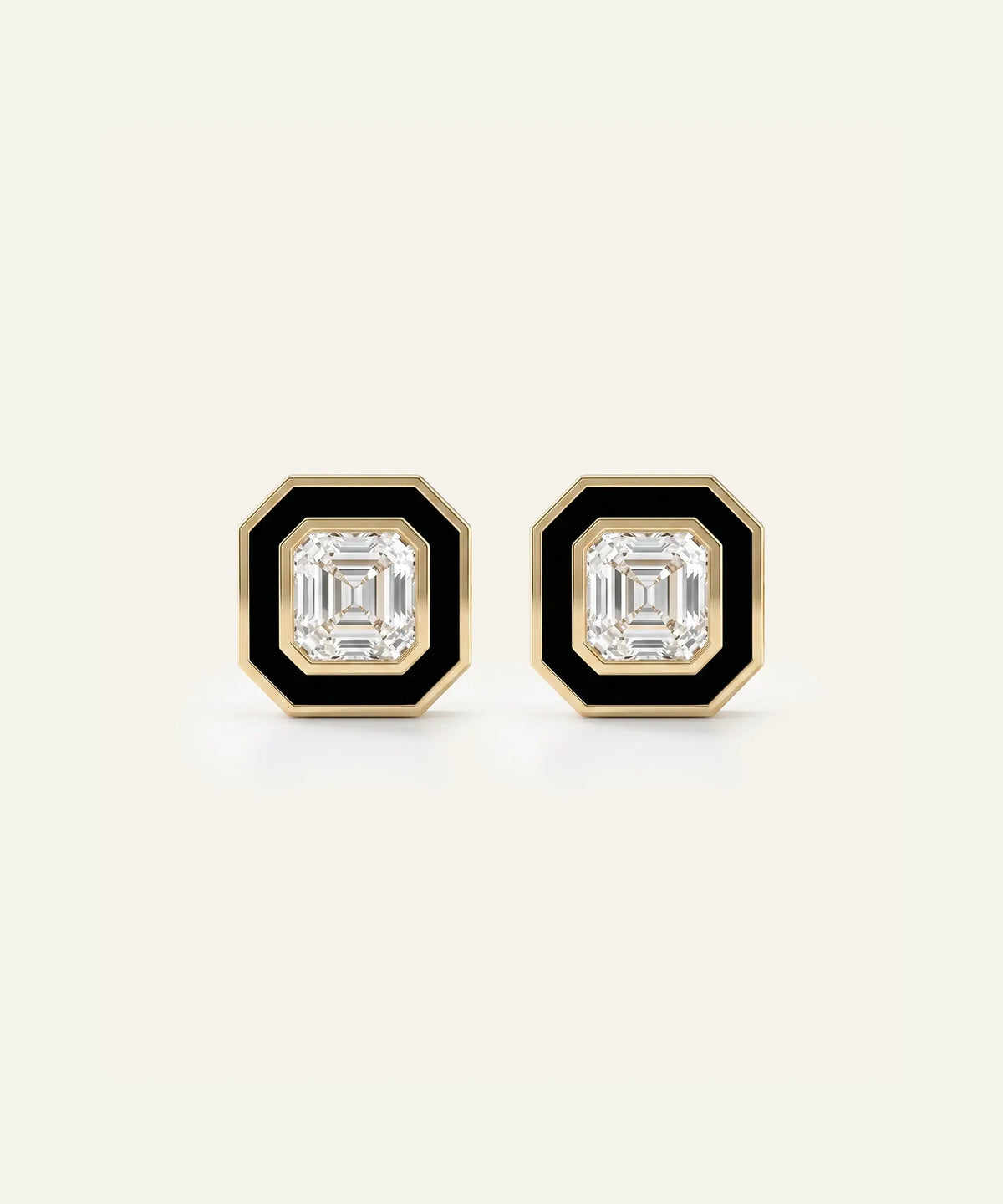 A pair of men's gold-toned stud earrings featuring square Asscher-cut clear central stones framed by black enamel borders, set against a light cream background.