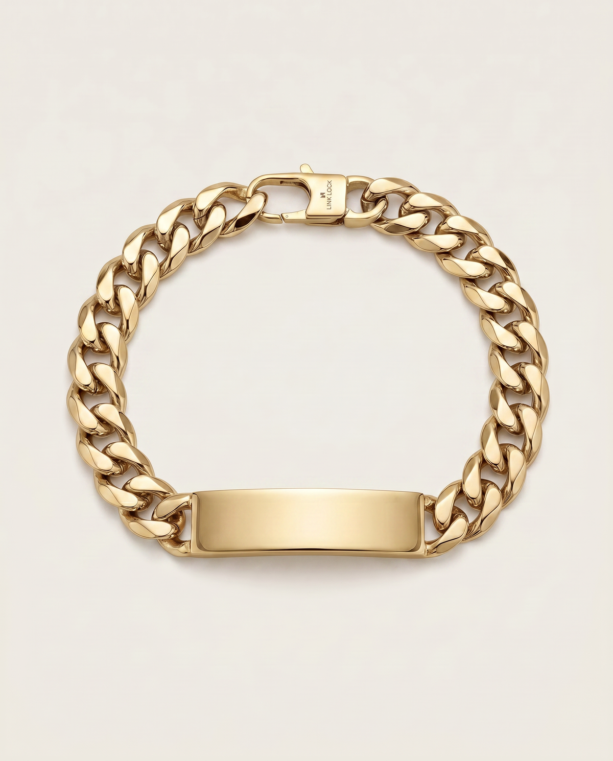 A gold-tone Cuban link chain bracelet with a polished rectangular ID plate, shown on a light beige background.