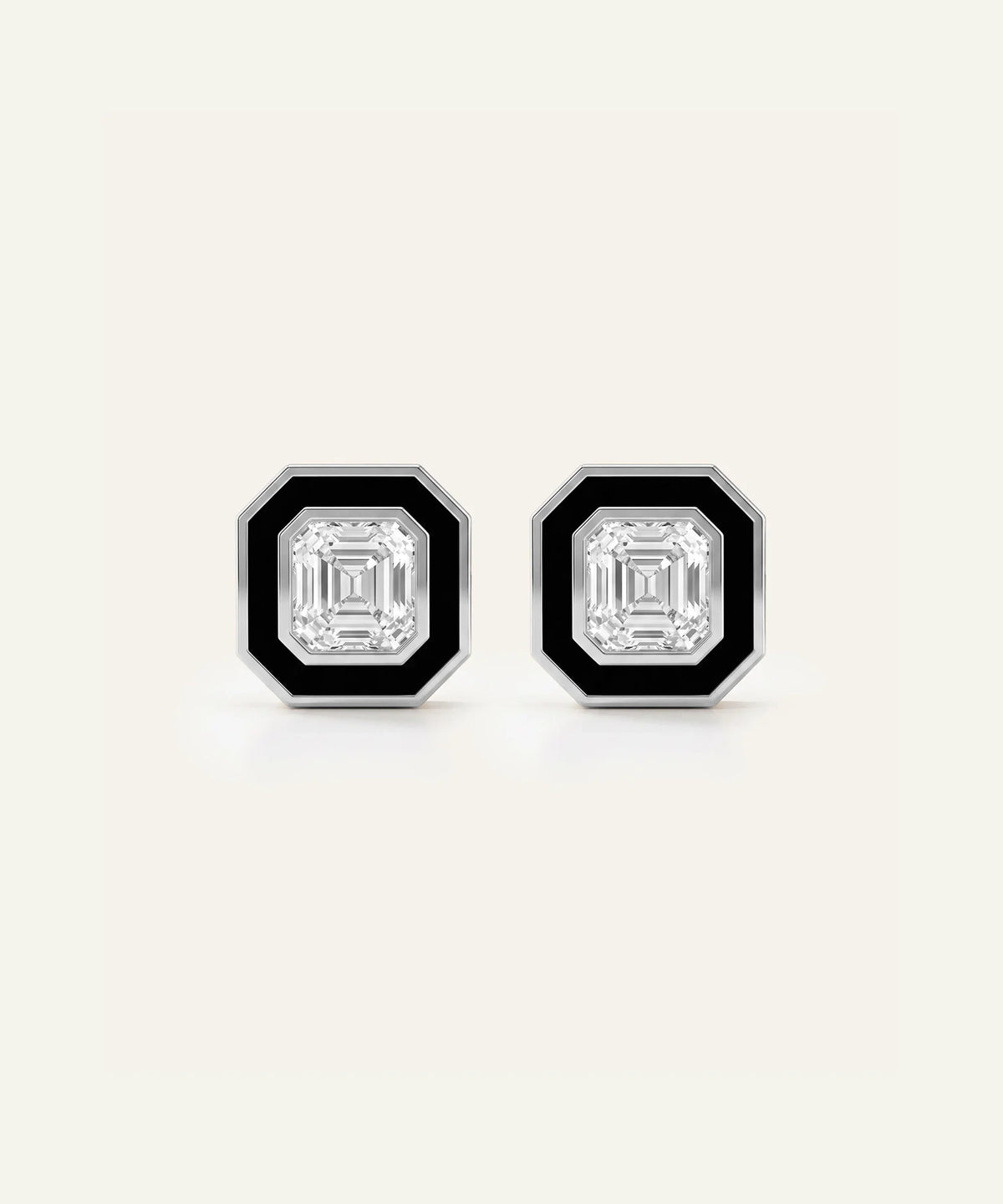 A pair of men's silver stud earrings featuring square Asscher-cut clear central stones framed by black enamel borders, set against a light cream background.