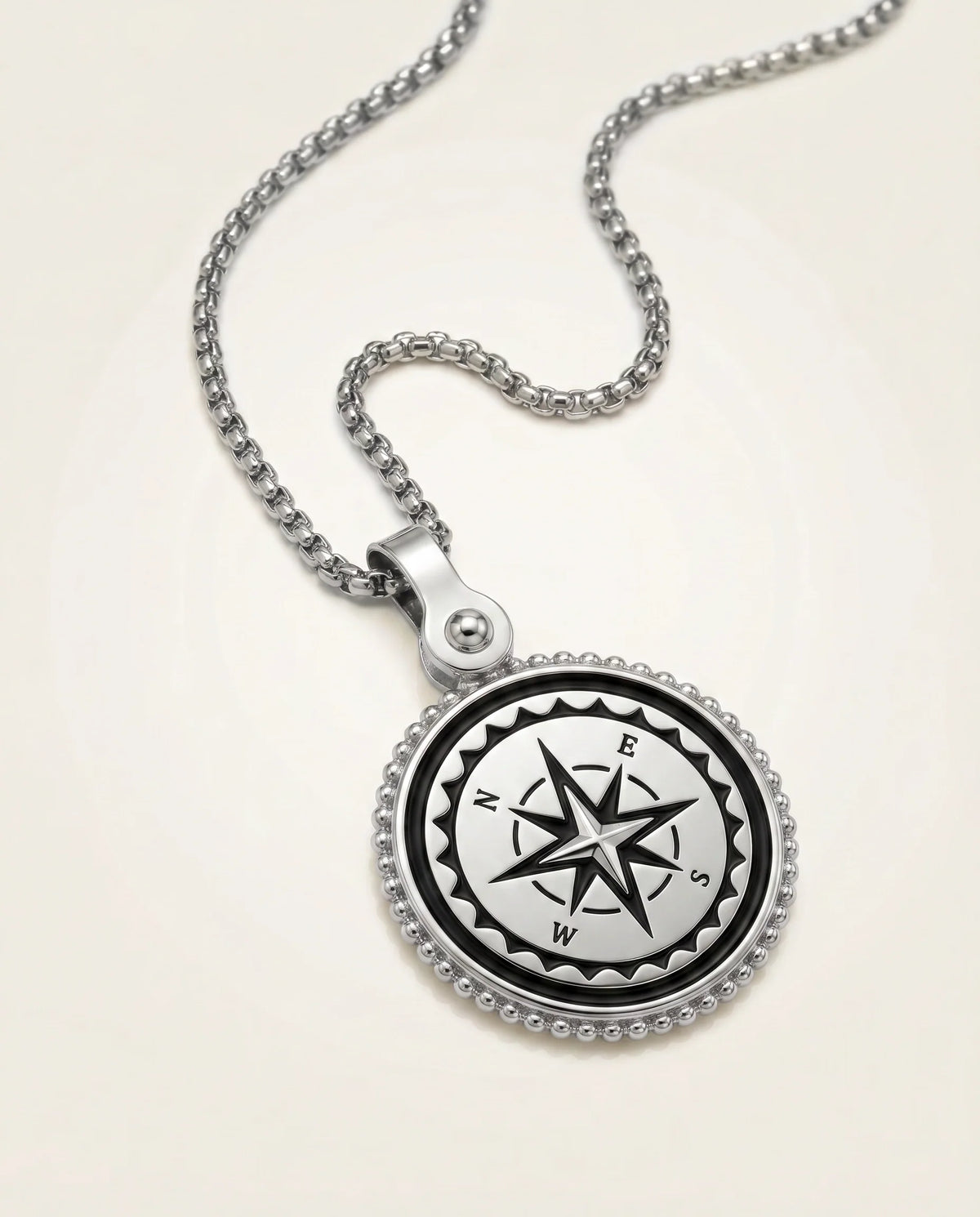 A silver compass pendant necklace on a matching silver box chain, displayed on a clean, light beige background.