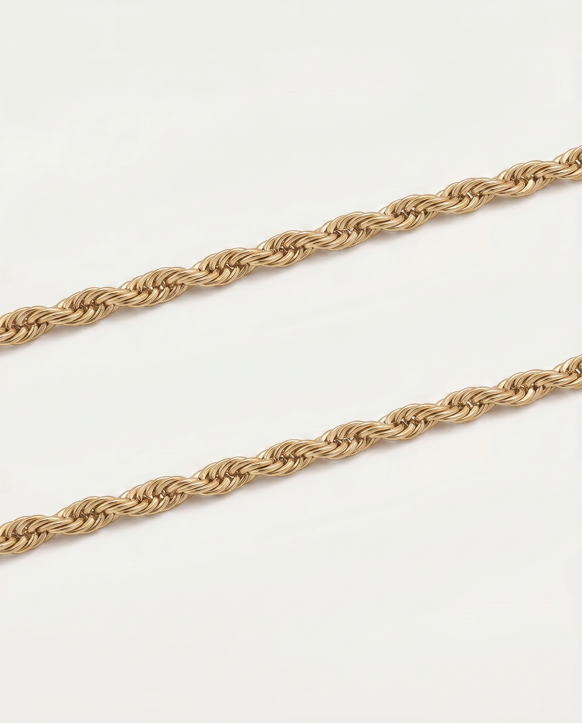 A close-up of a twisted rope chain necklace in a warm gold tone, laid diagonally across a plain white background.