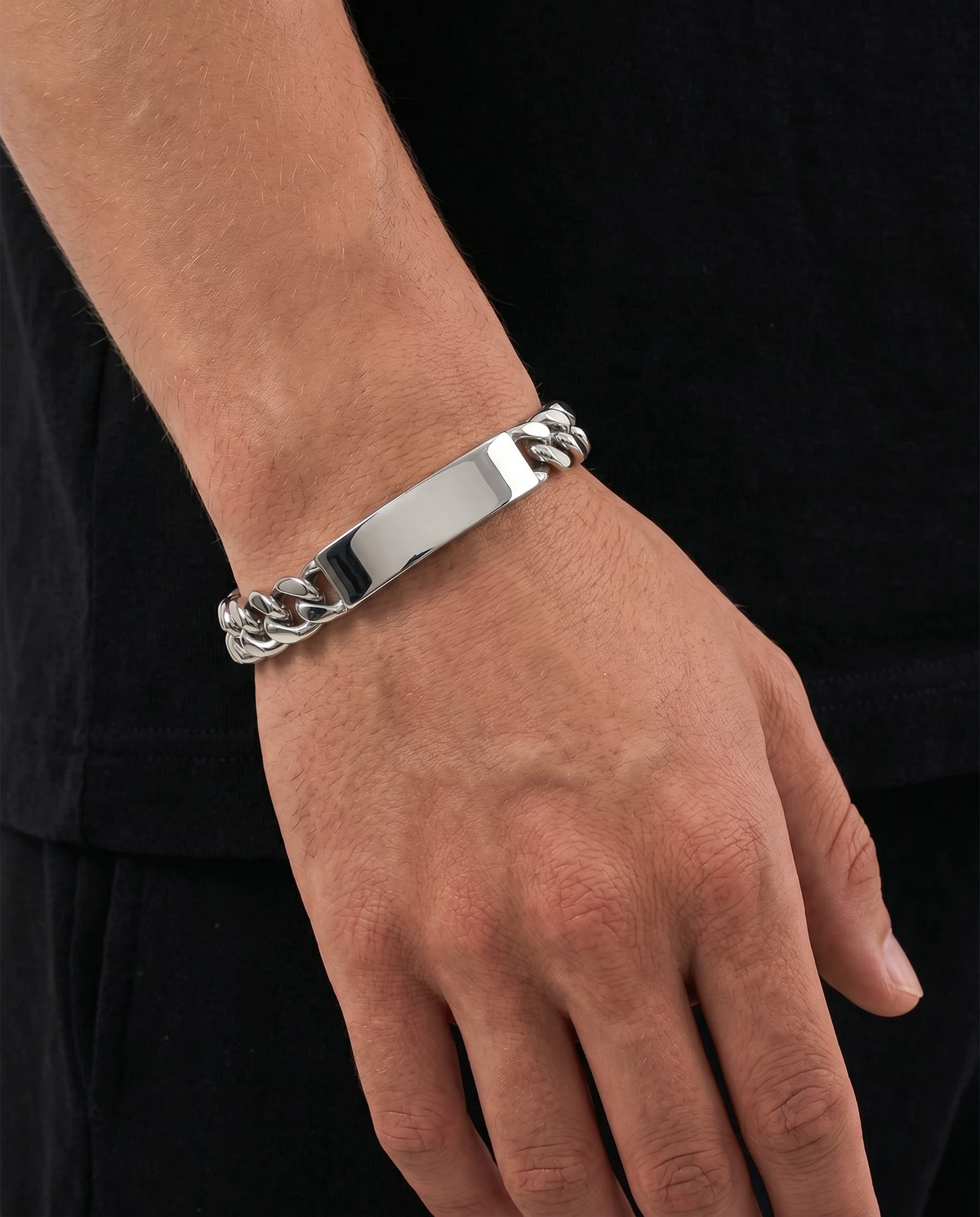 A silver-toned metal ID bracelet with a polished central bar and curb-link ends, shown worn on a person's wrist against a black shirt background.