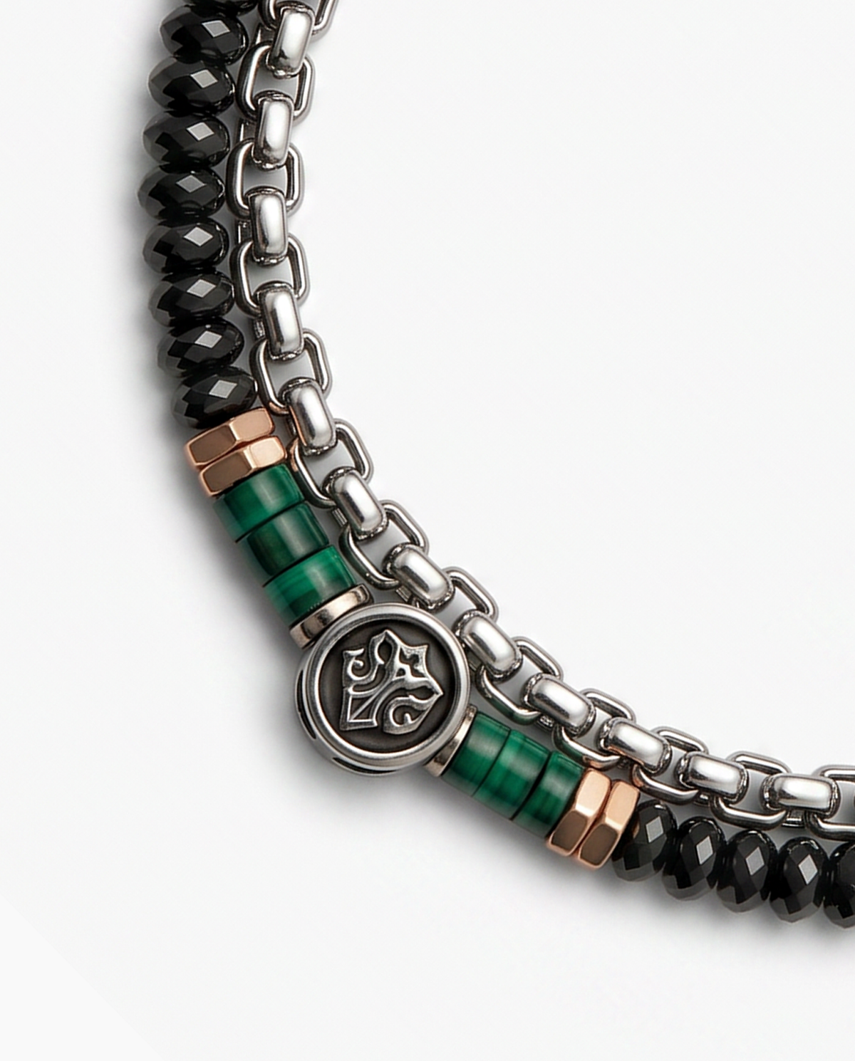A close-up of a multi-strand statement necklace featuring a silver chain, faceted black beads, and green malachite cylindrical accents with rose gold end caps, on a light gray background.