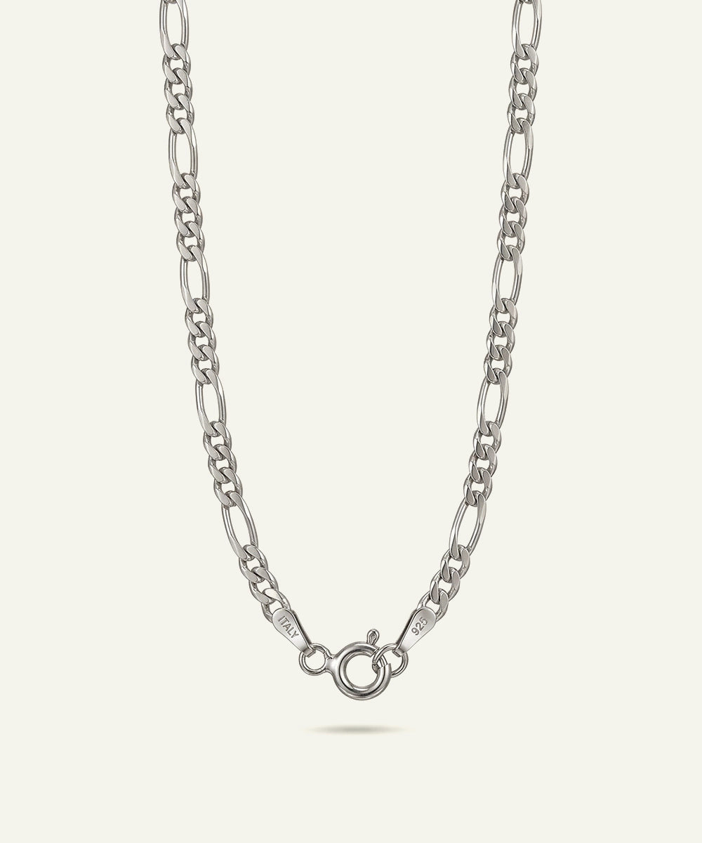 A silver Figaro chain necklace with a lobster clasp, shown against a light cream background.