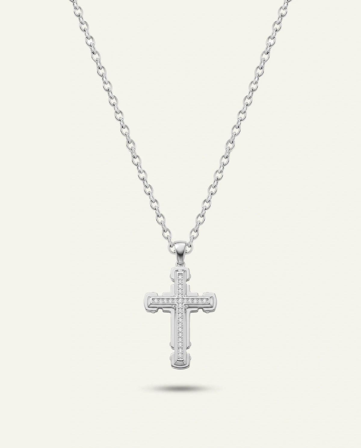 A silver cross pendant necklace with a delicate chain, shown against a light cream background with a soft shadow underneath.