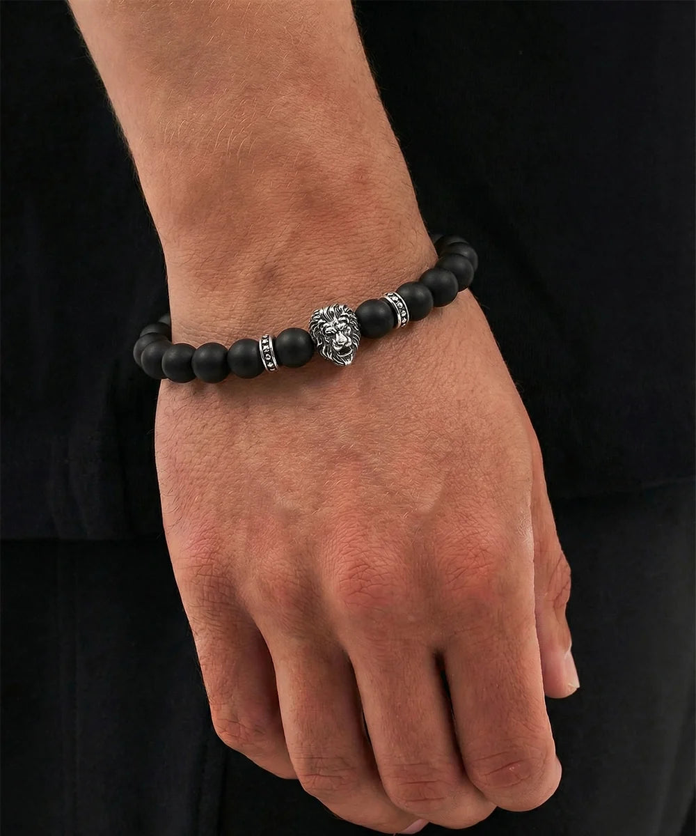 Hand wearing a black beaded bracelet with a silver lion clasp on a black background