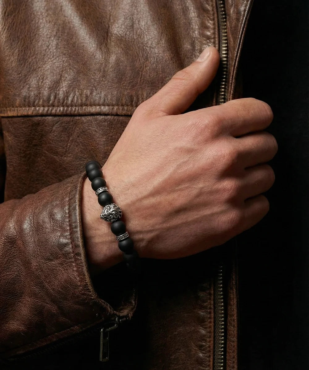 Hand wearing a black beaded bracelet with a brown leather jacket