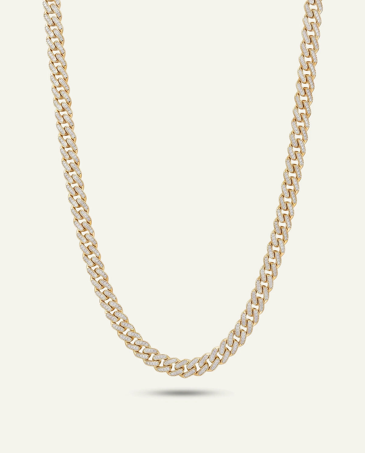 A gold-toned Cuban link chain necklace displayed in a curved U-shape against a light cream background.