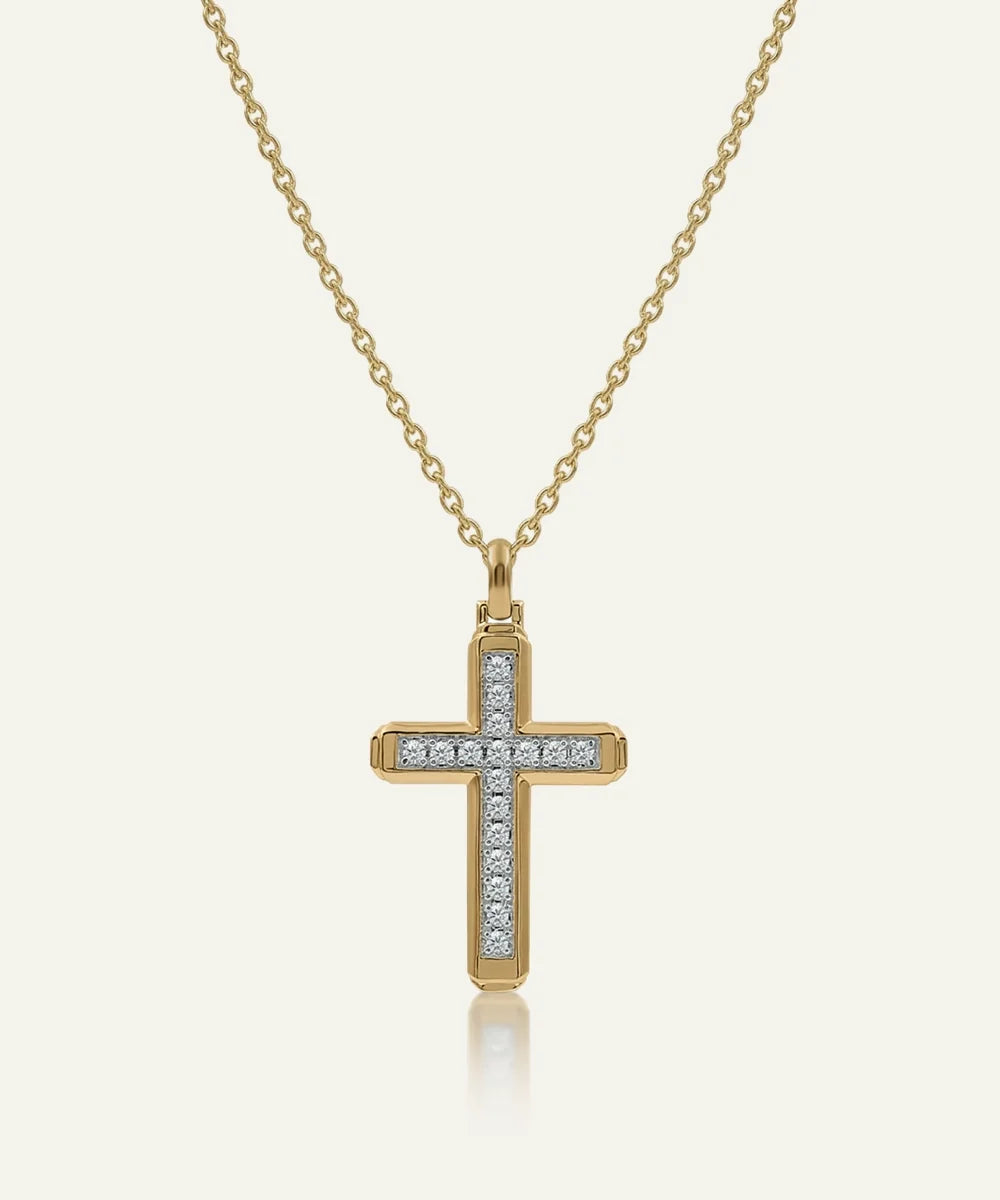 A gold cross pendant necklace adorned with small clear stones along the horizontal and vertical bars, suspended from a delicate gold chain against a light cream background.