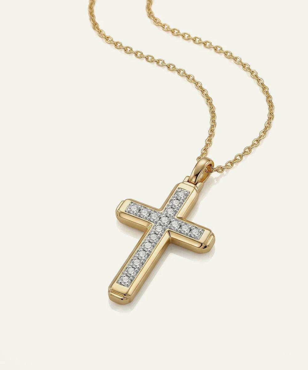 A gold cross pendant necklace adorned with small clear stones along the arms, suspended from a delicate gold chain against a light cream background.