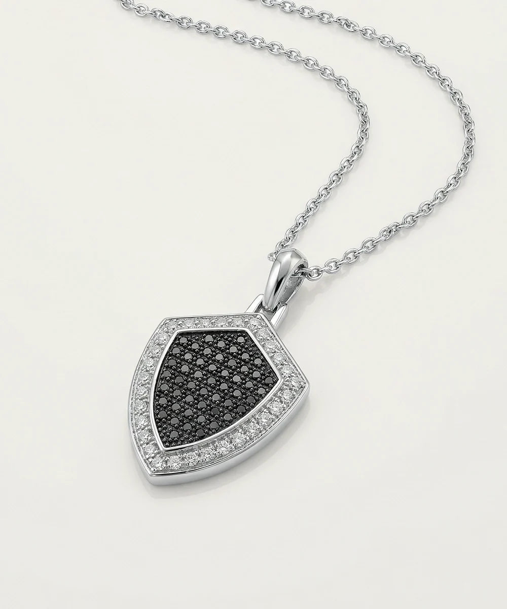 A silver shield-shaped pendant necklace featuring a black diamond-pattern center and a border of small clear stones, displayed on a clean white background.