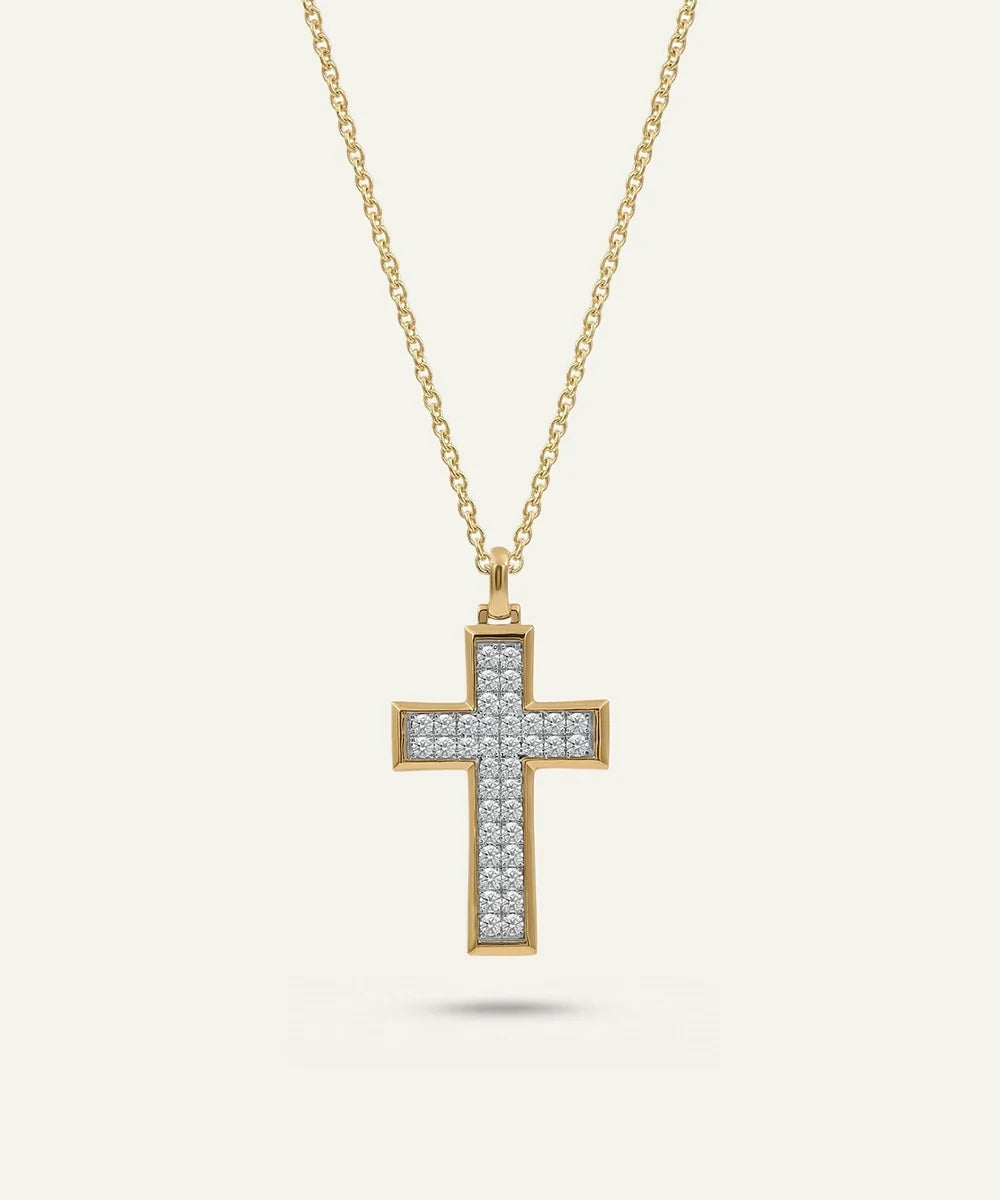 A gold cross pendant necklace adorned with small clear stones, suspended from a delicate gold chain against a light cream background.