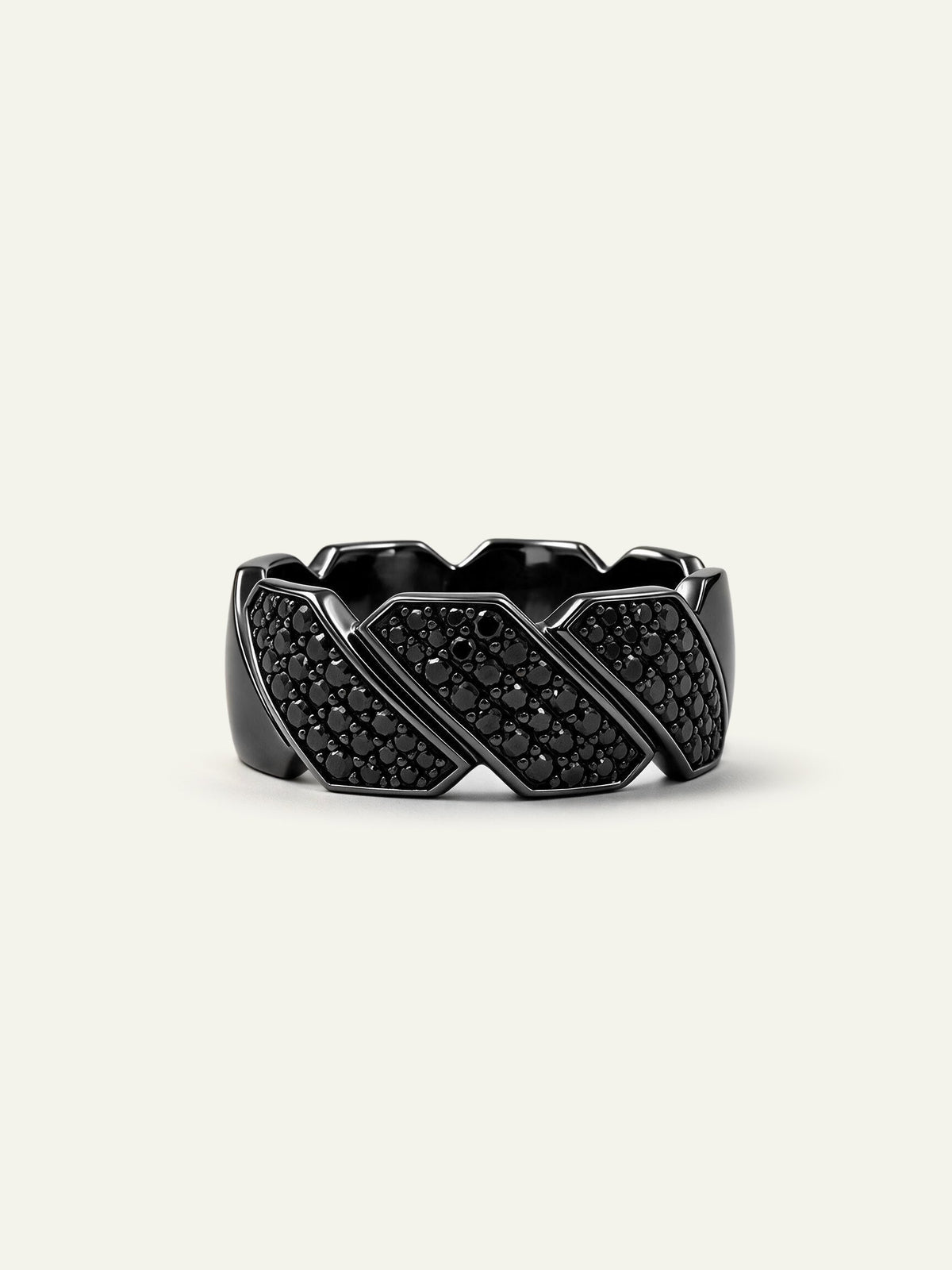 A wide men's black ring featuring a segmented geometric band accented with dark pavé-set black diamonds, displayed on a light cream background.