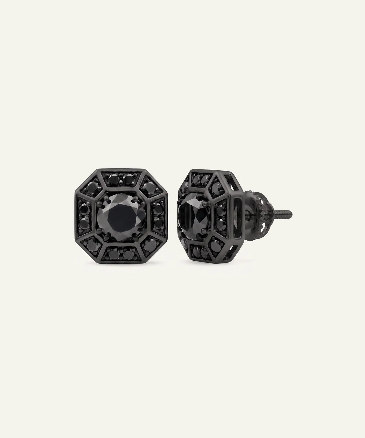 A pair of men's black stud earrings featuring round black central stones surrounded by patterned geometric frames set with black pavé stones, displayed on a light cream background.