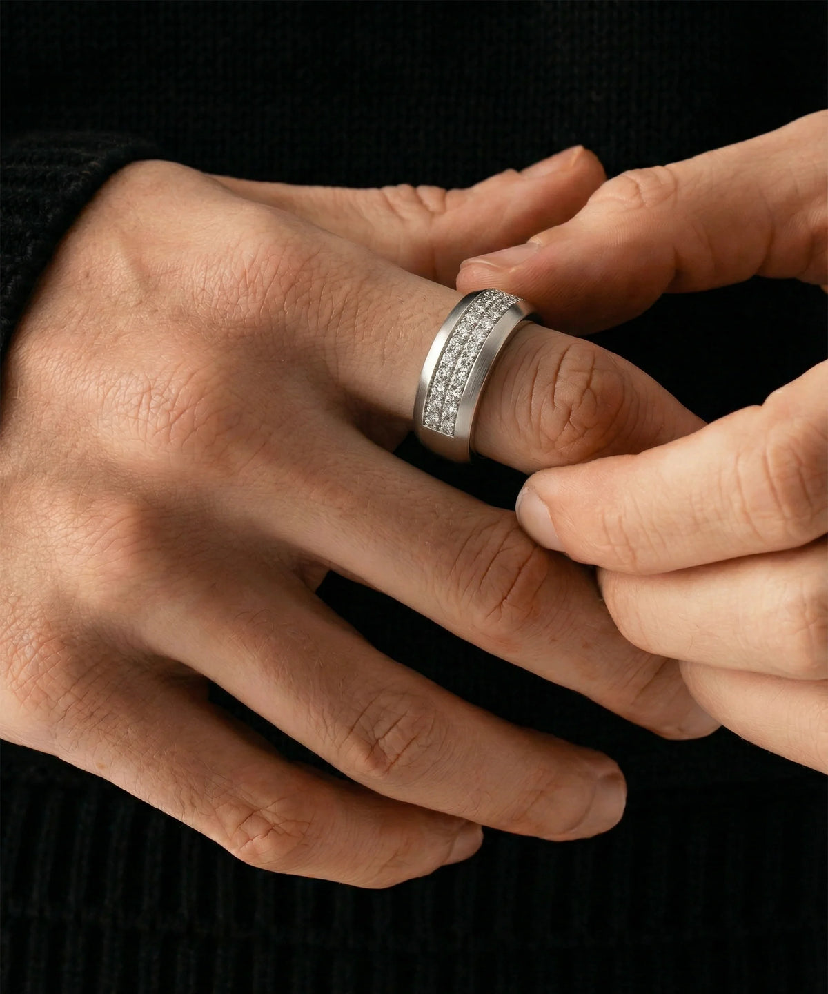A person adjusting a men's silver two-row diamond band ring on their finger against a dark background.