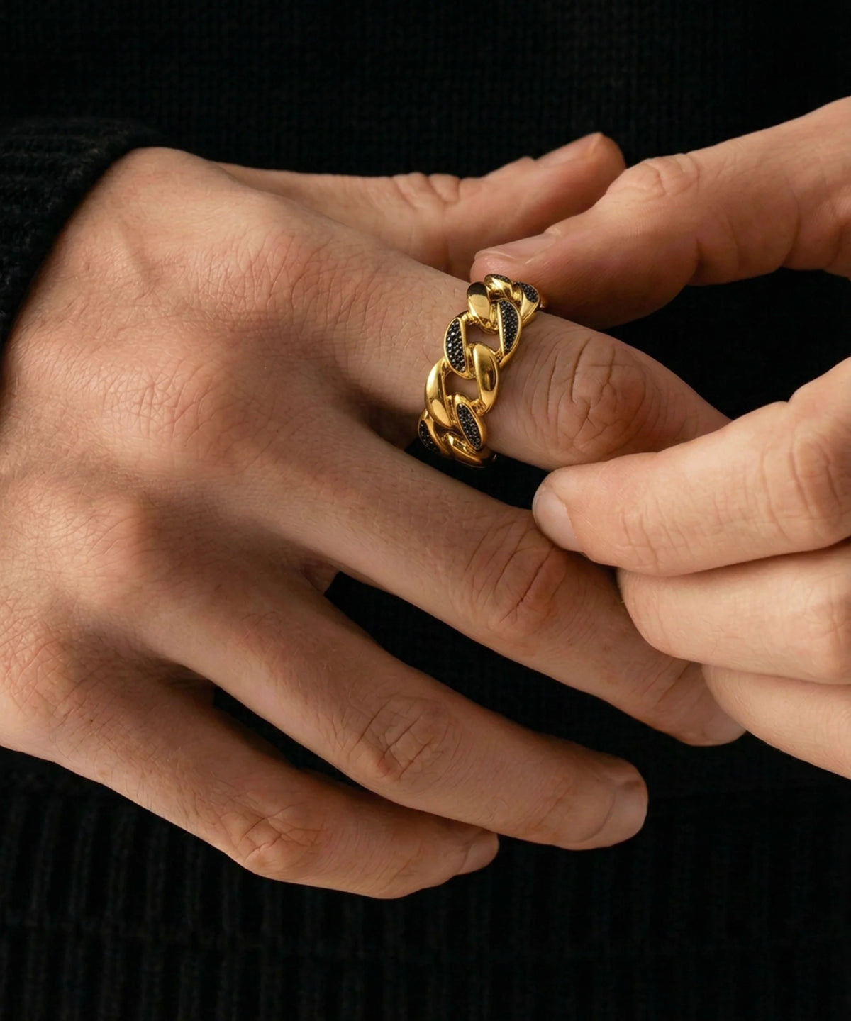 A person adjusting a men's yellow gold Cuban link ring set with black stones on their finger against a dark background.