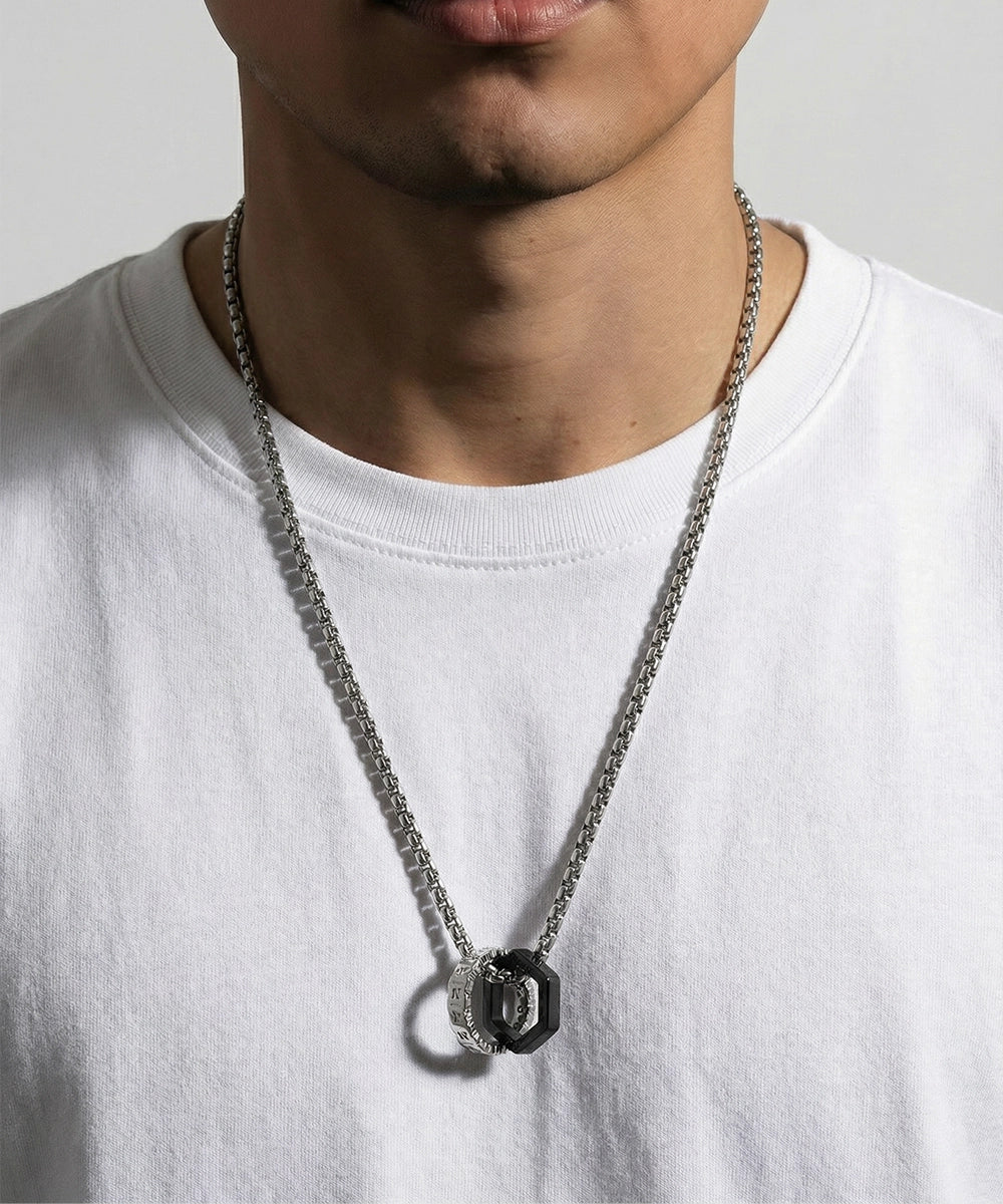 Person wearing a silver chain necklace with a black pendant on a plain background