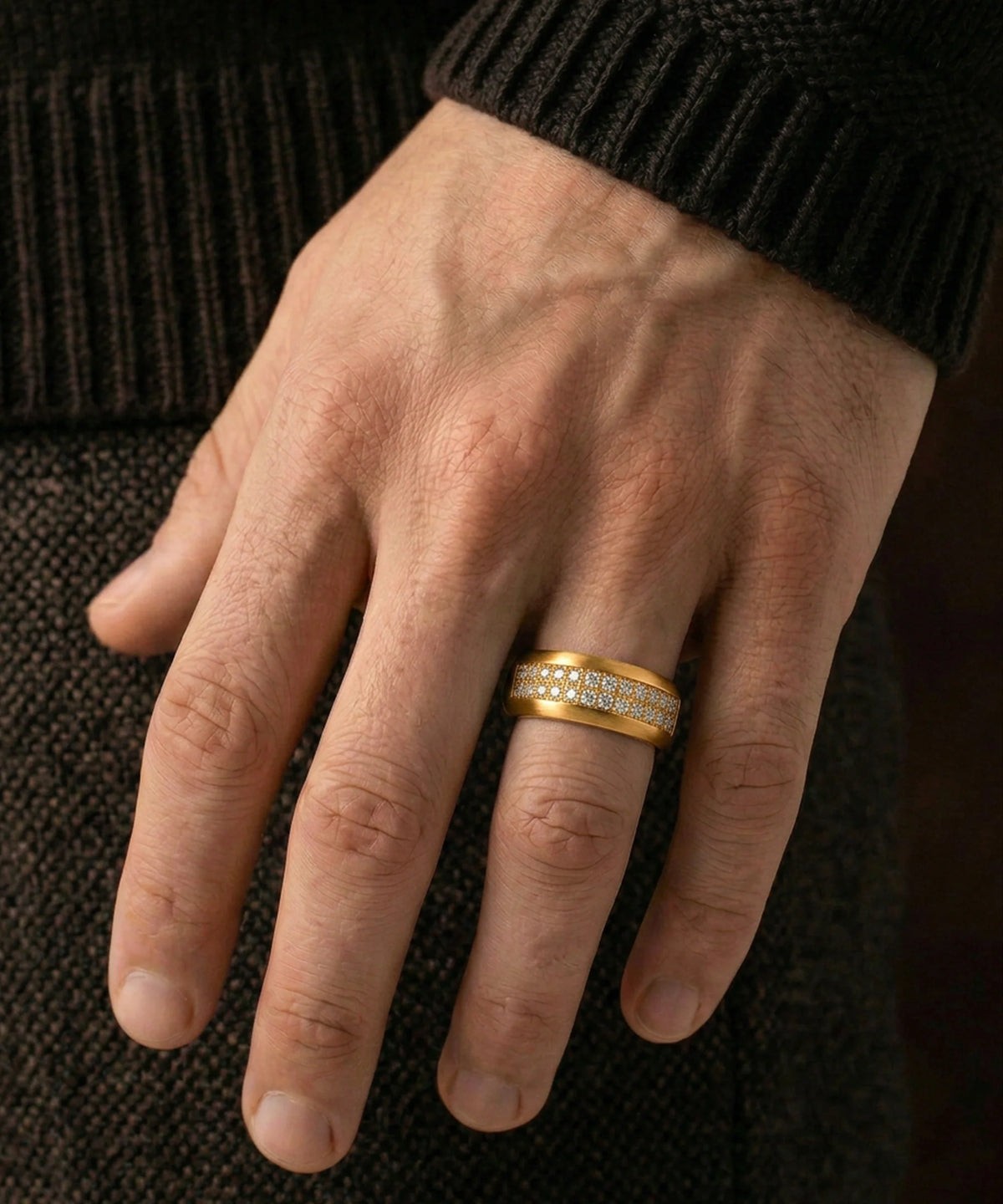 A person's hand wearing a men's yellow gold two-row diamond band ring against a dark background.