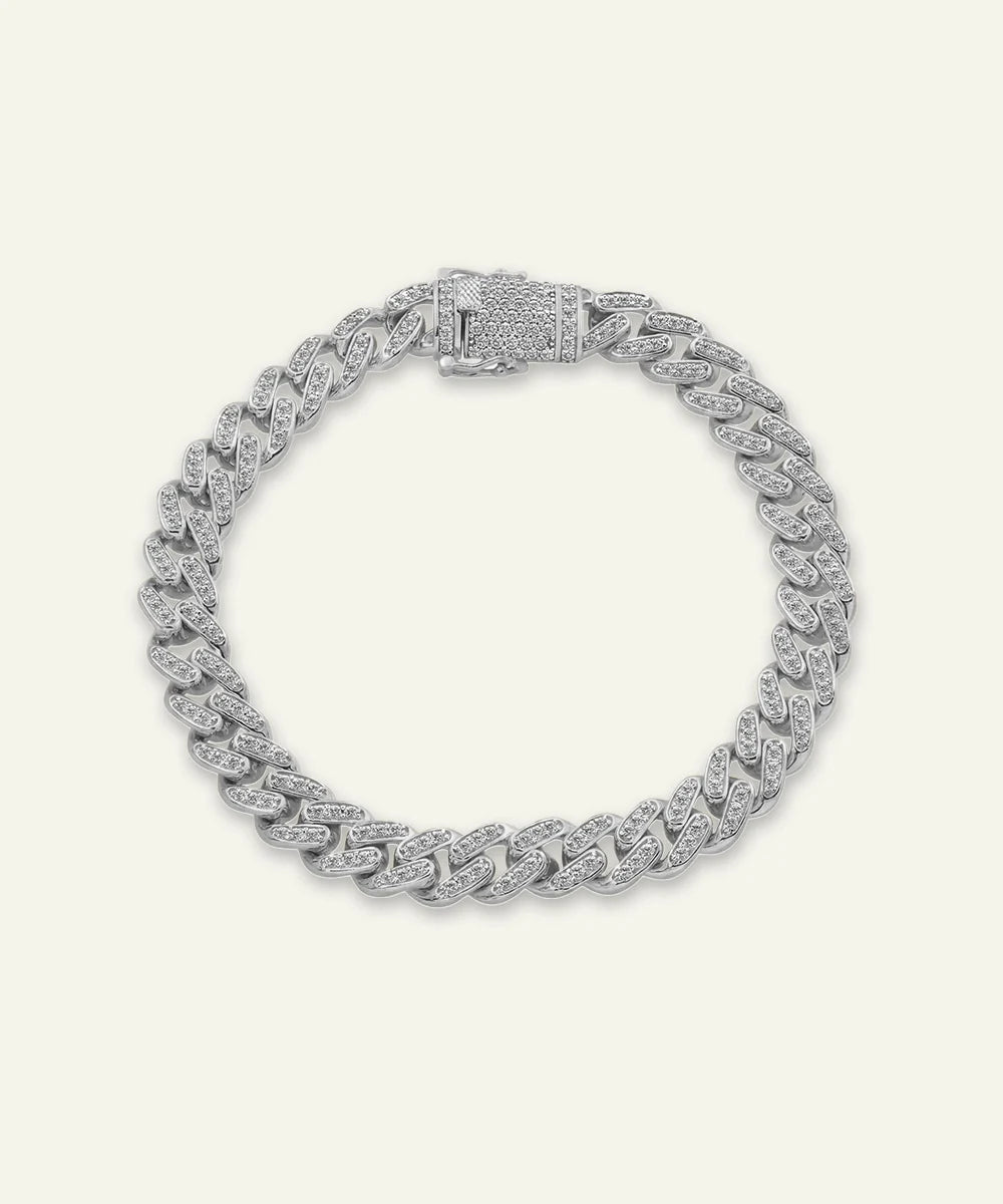 A silver-toned pavé diamond-encrusted Miami Cuban chain bracelet with a decorative clasp, displayed on a light cream background.
